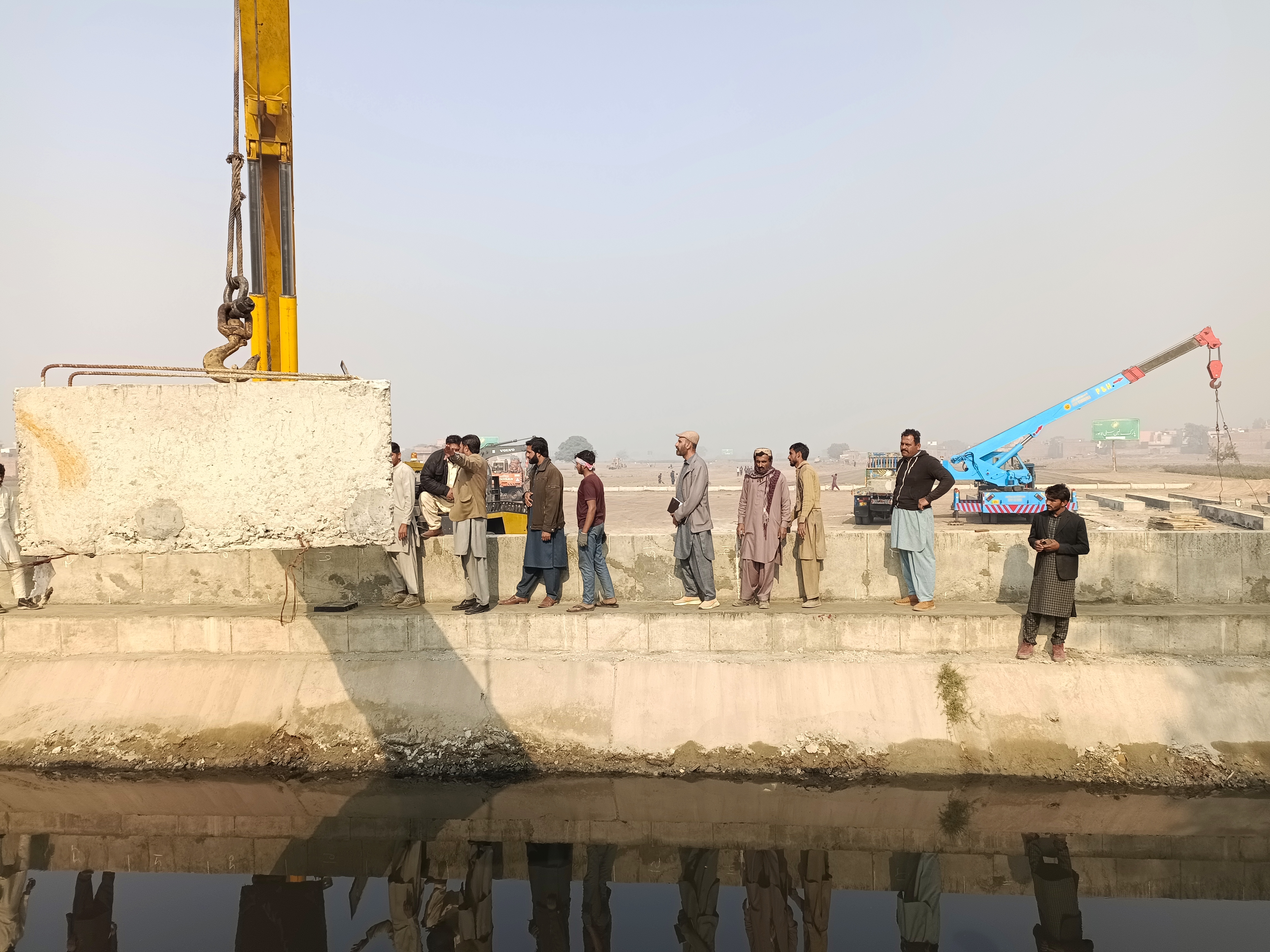 Construction workers and cranes laying concrete boundary wall foundations, December 2022