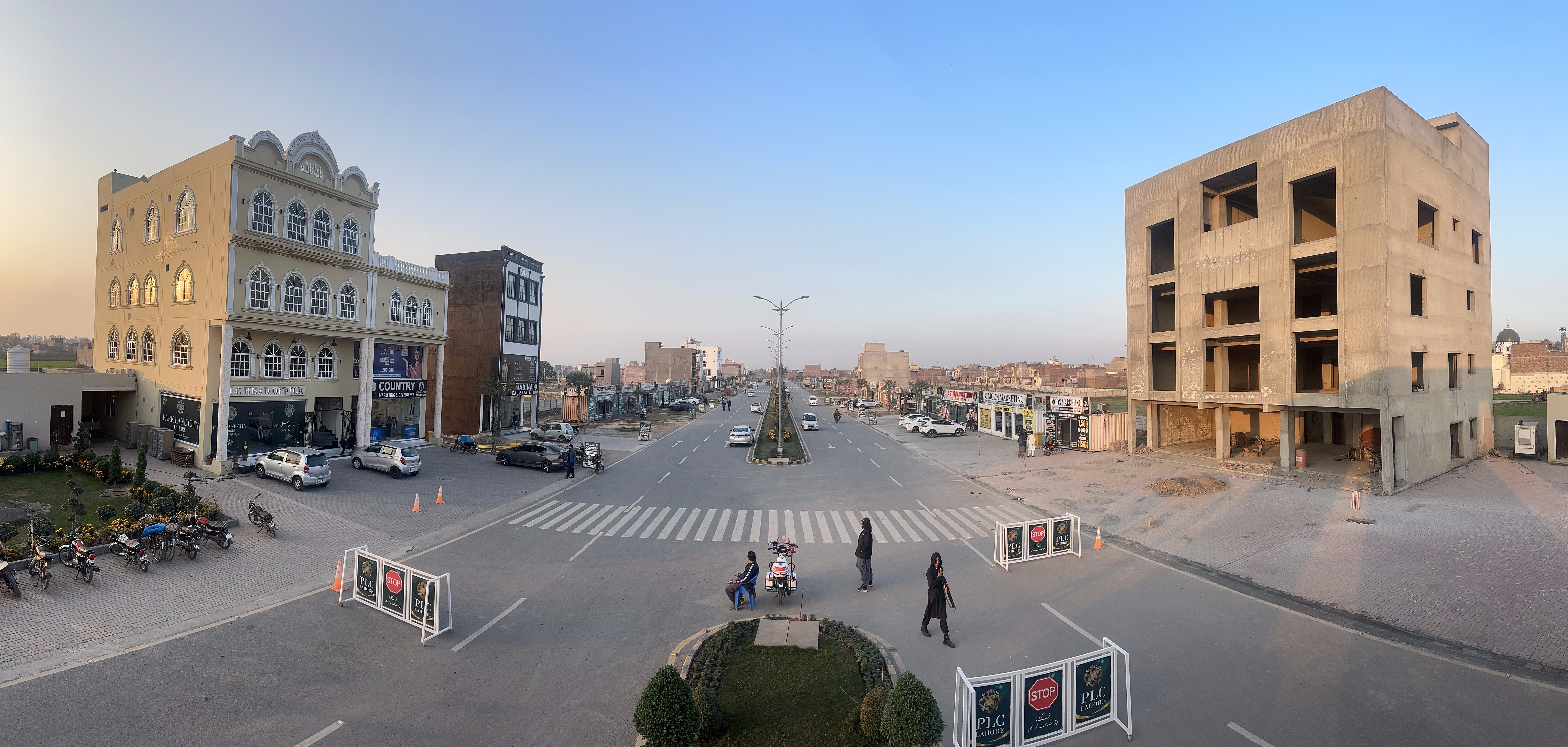 Panoramic view of Park Lane City commercial zone at dusk — established shops, offices, and the main roundabout with residents